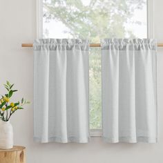 a white window curtain with ruffles hanging in front of a wooden table next to a potted plant