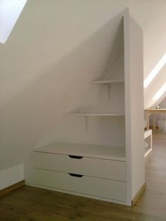 an attic bedroom with white furniture and open shelves on the wall, along with hardwood flooring