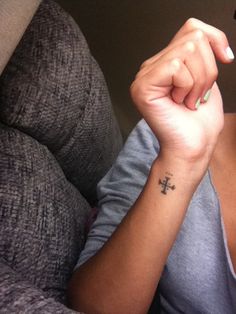 a woman with a small cross tattoo on her left arm, sitting in a chair