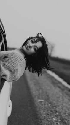 black and white photograph of woman leaning out the window of car on road with sky in background