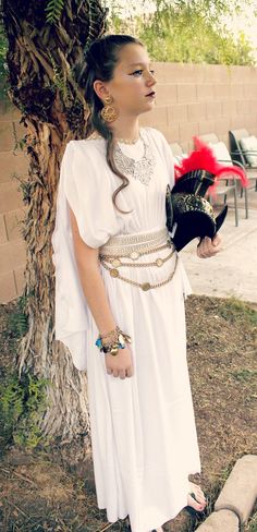 a woman in a white dress standing next to a tree