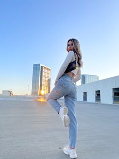 a woman standing on one leg in the middle of an empty parking lot with buildings in the background