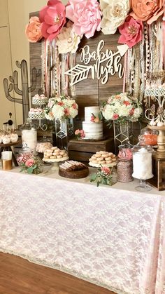 a table topped with lots of cakes and desserts next to a wall covered in paper flowers