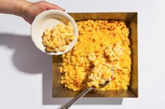 a person holding a spoon over a bowl of macaroni and cheese