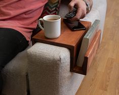 a person sitting on a couch with a remote control in their hand and a cup of coffee