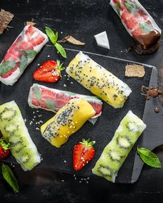 various fruits and vegetables wrapped in rice on a cutting board with mint leaves, strawberries, and chocolate