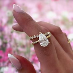 a close up of a person's hand holding a ring with a pear shaped diamond on it