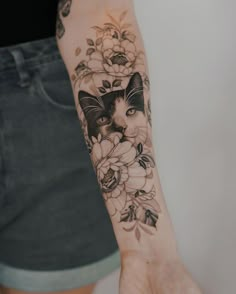 a woman's arm with a cat and flowers tattoo on her left arm,