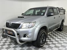 a silver pick up truck is parked in a checkerboard floored room with black and white tiles