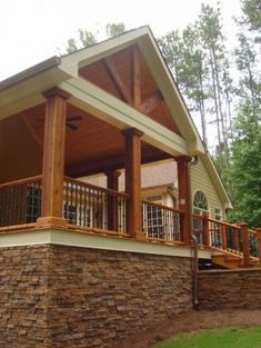 a wooden porch with stone walls and railings on the front of a house in the woods