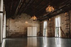 an empty room with chandeliers and windows in the center, surrounded by brick walls