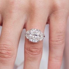 a woman's hand with a diamond ring on top of her finger and the other hand holding an engagement ring