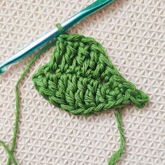 a green crochet piece sitting on top of a table next to a ball of yarn