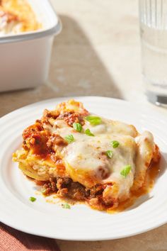 a white plate topped with lasagna covered in cheese and sauce next to a glass of water