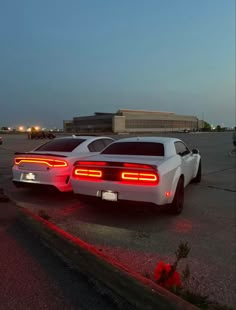 two white sports cars parked next to each other in an empty parking lot at night