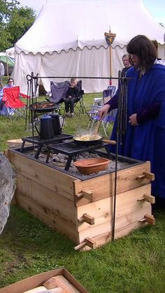 a woman cooking food on top of a grill in the grass next to a tent