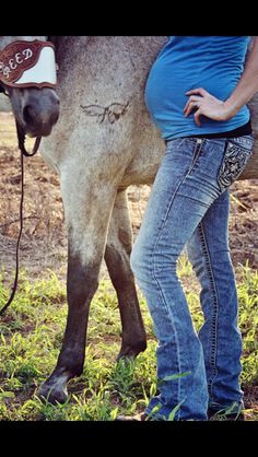 a pregnant woman standing next to a horse