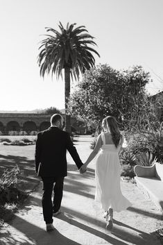 black and white photo of bride and groom walking hand in hand through the desert with palm trees