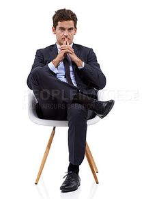 a man in a suit sitting on a chair with his hands clasped to his mouth