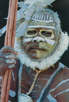 a man with painted face holding a stick and wearing feathered headdresses