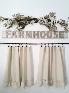 the curtains are hanging in front of the sign that says farmhousee and flowers hang on the wall