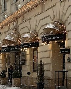 people are walking on the sidewalk in front of a building covered with lights and snow