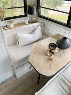 a living room with white couches and wooden table in front of two large windows