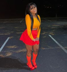 a woman standing in a parking lot at night wearing red and yellow clothing with orange socks