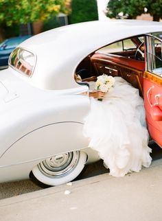 a woman in a wedding dress is sitting on the back of a red and white car