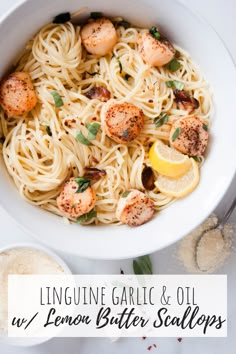 a white bowl filled with pasta and scallops on top of a table next to garlic