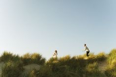 couple running on grassy dunes Engagement Photos Moody, Ocean Photoshoot, Movement Poses, Couples Beach Photoshoot, Morro Bay California, Beach Poses For Couples, Blurry Photos, Couples Pose, Photography Cinematic