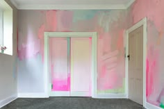 an empty room with pink and blue paint on the walls, two doors open to another room