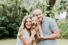 a man and woman holding a puppy in their arms while posing for a photo with trees in the background