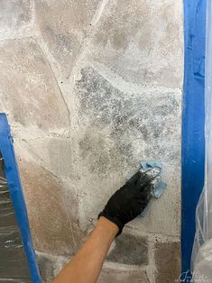 a person with black gloves is painting a stone wall in the process of remodeling