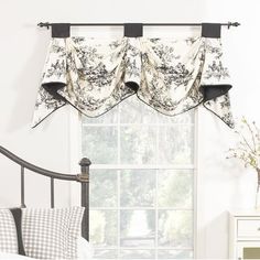 a bedroom with a bed, window and dresser in it's corner area that has a black and white floral valance hanging over the headboard