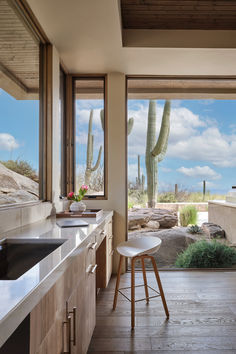 a kitchen with wooden floors and white counter tops next to a large window that looks out onto the desert