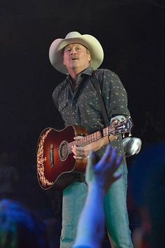 a man wearing a cowboy hat and holding a guitar in front of an audience at a concert