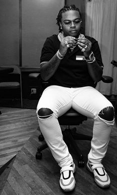 a black and white photo of a man sitting on a chair with his hands clasped