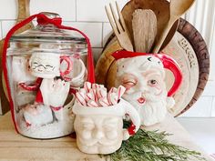 two santa clause figurines sitting on top of a counter next to a jar filled with candy canes