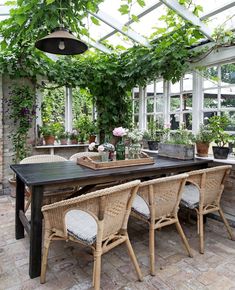 an outdoor dining area with wicker chairs and table surrounded by greenery on the roof