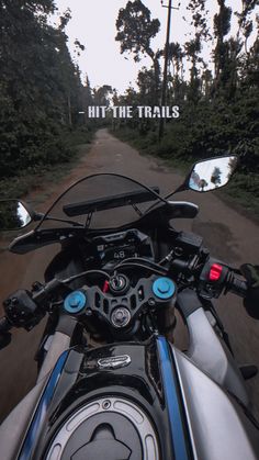 the front view of a motorcycle driving down a dirt road with trees in the background