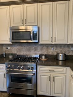 a stainless steel stove and microwave in a kitchen with granite counter tops, white cabinets and silver appliances