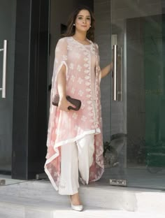 a woman standing on steps in front of a glass door wearing a pink top and white pants