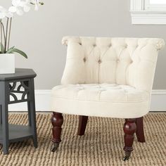 a white chair sitting on top of a rug next to a vase with flowers in it