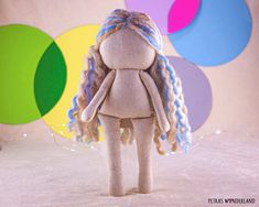 a stuffed doll with blue hair standing in front of colorful circles