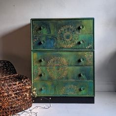 a green dresser sitting next to a basket with christmas lights on it and a small tree in the corner