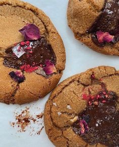 three cookies with chocolate and pink flowers on them sitting on top of a white surface