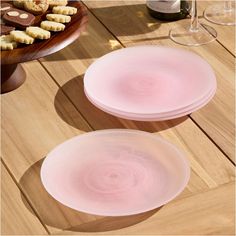 two pink plates sitting on top of a wooden table next to wine glasses and cookies