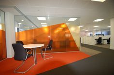 an office cubicle with glass partitions and orange carpeted flooring is shown