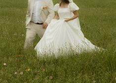 a bride and groom walking through the grass